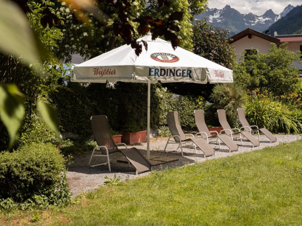 Der Sommer darf kommen! Garten mit Liegestühlen und Sonnenschirm vor Bergen im Hintergrund.