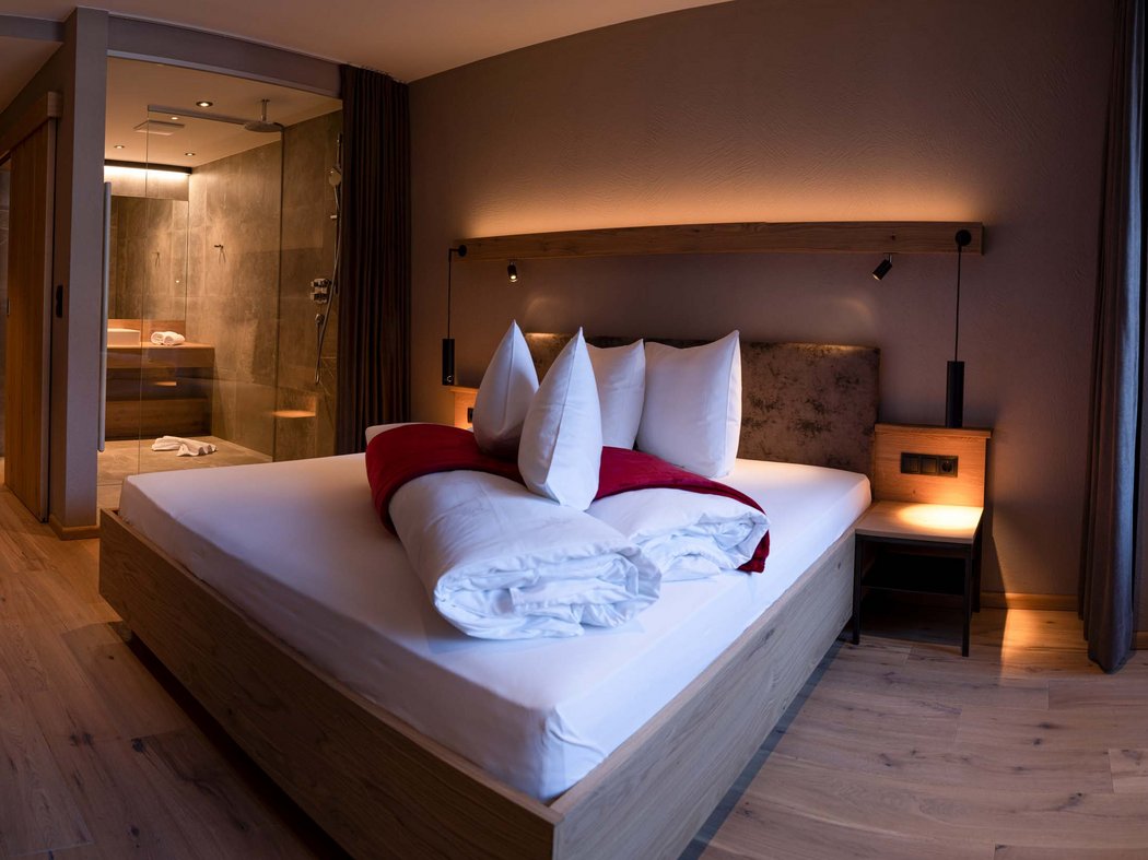 Junior Suite Modernes Schlafzimmer mit Holzboden, Bett und offener Dusche im Hintergrund