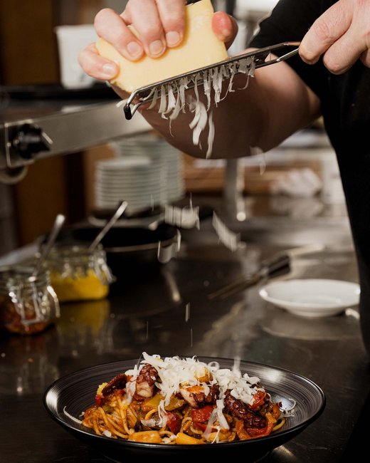 Ihr Wohlfühlort: das Hotel in Prutz im Tiroler Oberland ⛰️ Hand reibt Käse über einen Teller mit Pasta und Meeresfrüchten
