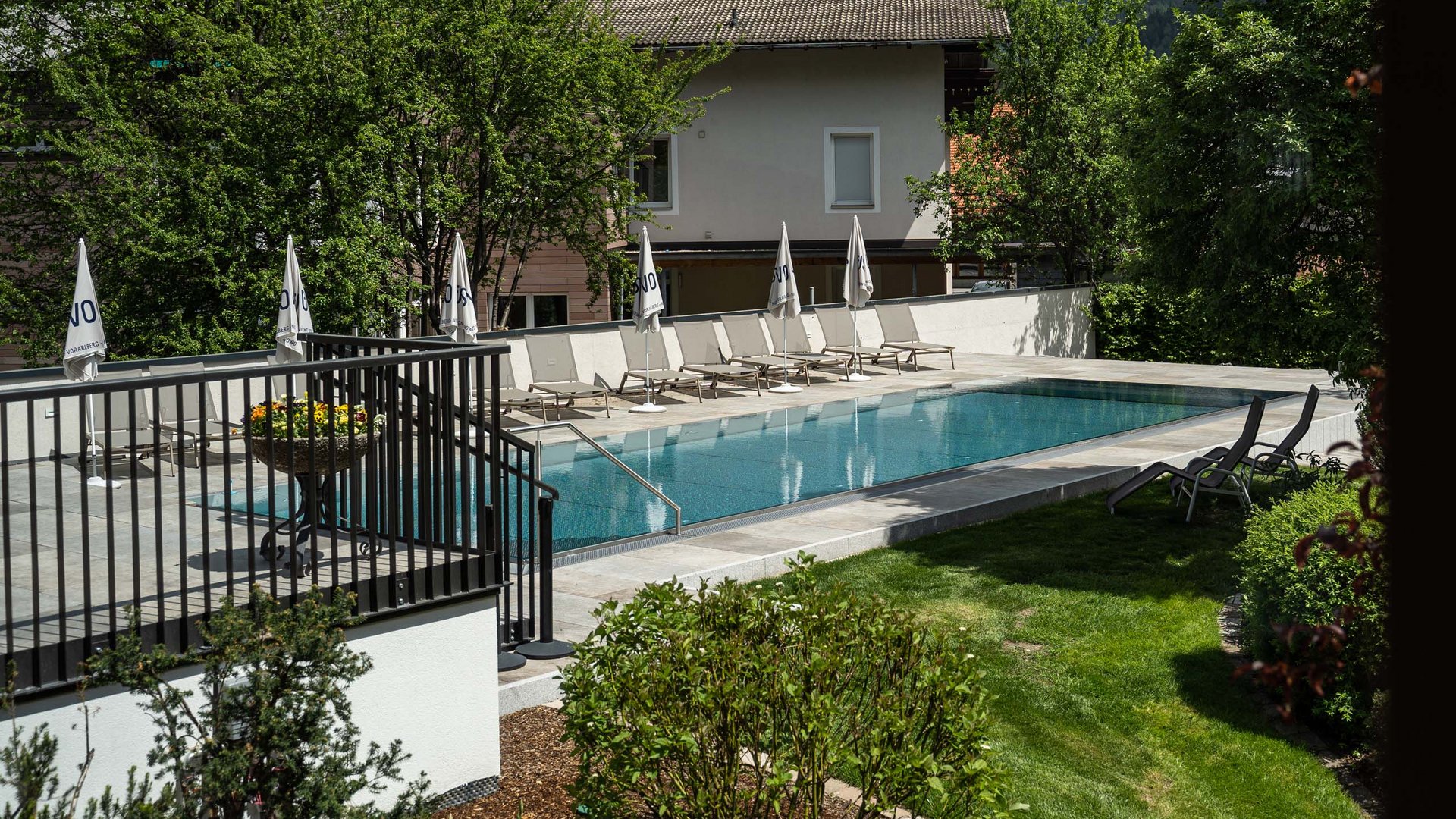 Outdoorpool Außenpool mit Liegestühlen und Sonnenschirmen neben einem Haus und Garten