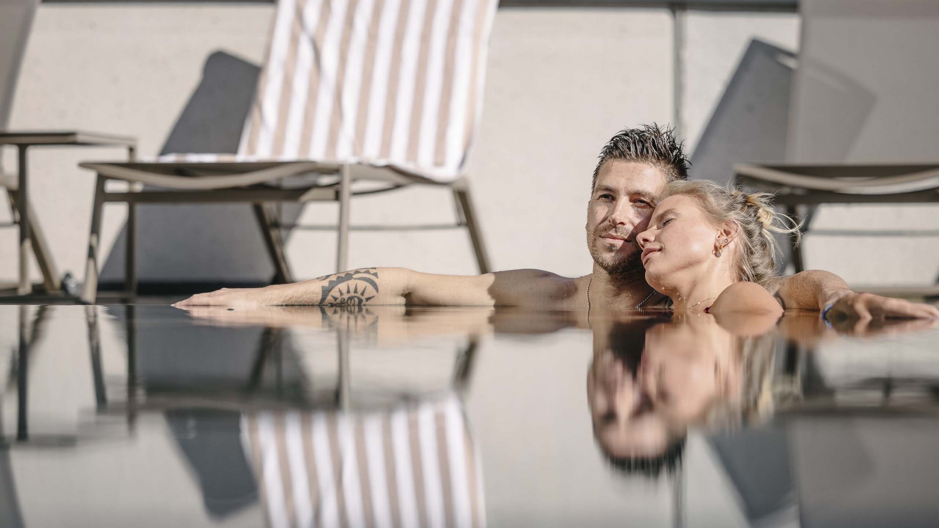 Looking for a hotel with spa in Tyrol? Couple relaxing together in a pool with chairs and towel in the background