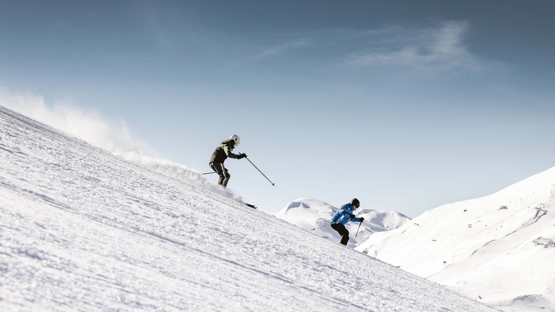 Zwei Skifahrer fahren einen verschneiten Hang bei klarem Himmel hinunter