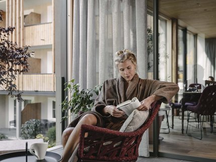 Looking for a hotel with spa in Tyrol? Woman reading book relaxed on balcony wearing bathrobe