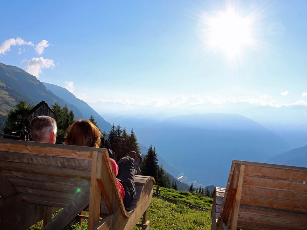5 Tipps für Wanderer in den Tiroler Bergen Zwei Personen liegen auf Holzbänken und genießen die Sonne in den Bergen