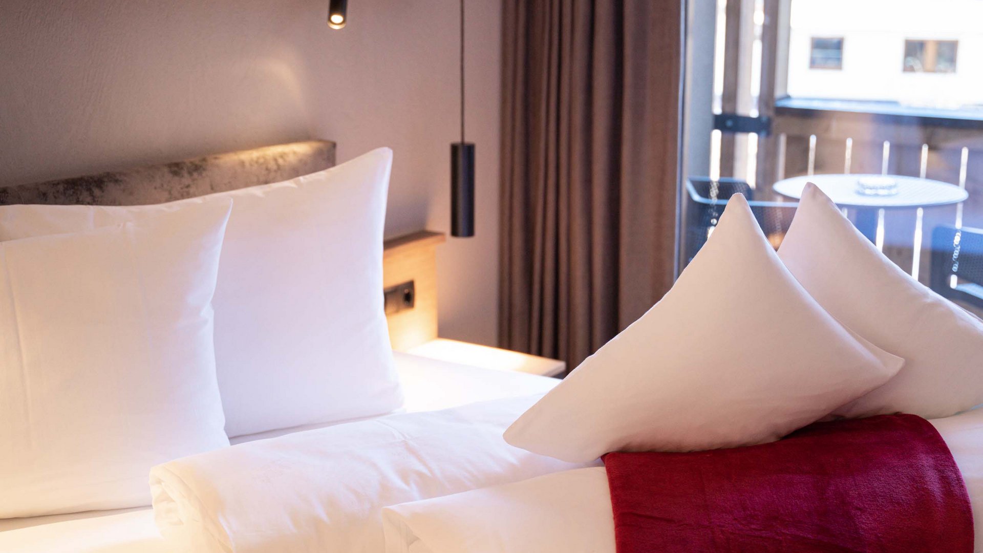 Your Tyrolean Oberland hotel Modern hotel room with white bedding and red accents near the window