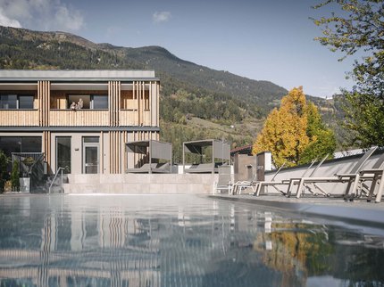 Ihr Urlaub im Sporthotel in Tirol Moderner Holzbau neben einem Pool mit Bergen und Herbstbäumen im Hintergrund