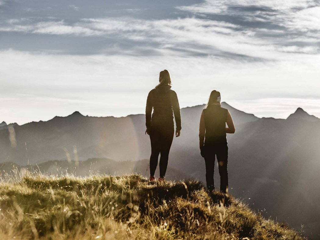 Autumn excursions near Prutz Two people standing on a grassy hill with mountain range in the background