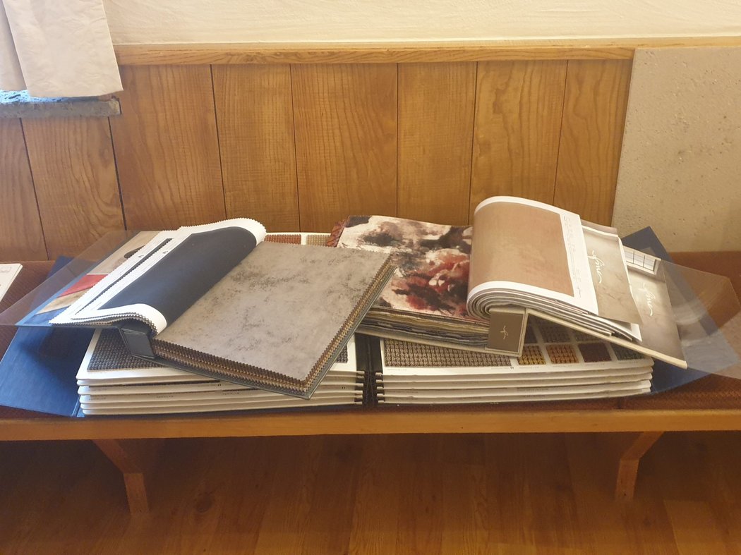 Nun geht es ans Einrichten Musterbücher mit Stoff- und Tapetenproben auf einer Bank mit Holzverkleidung