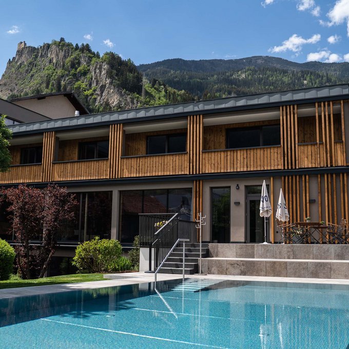 Hotel mit Sauna in Tirol Modernes Gebäude mit Holzfassade neben Pool vor bewaldeten Bergen