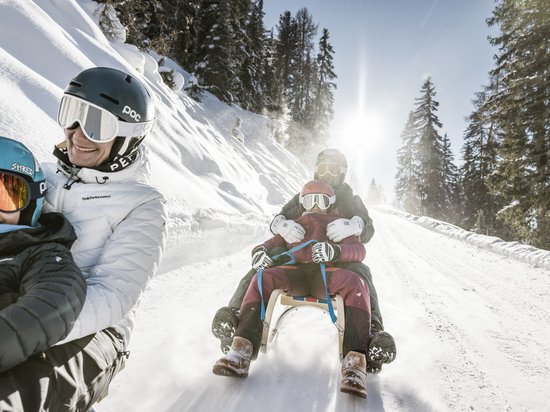 Echtes Kleinod aus dem Tiroler Oberland Mehrere Personen genießen Schlittenfahrt auf schneebedecktem Bergweg bei sonnigem Wetter