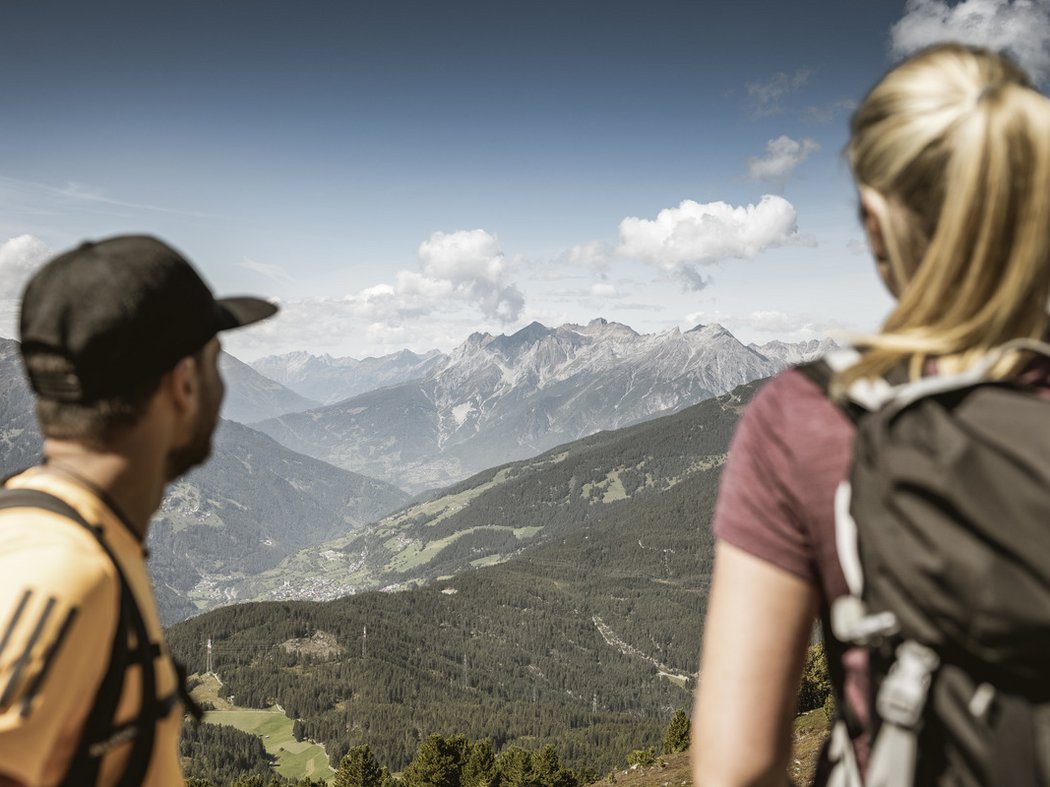 Wanderhotel Post Prutz Zwei Wanderer mit Rucksäcken blicken auf eine Berglandschaft mit bewaldeten Hügeln