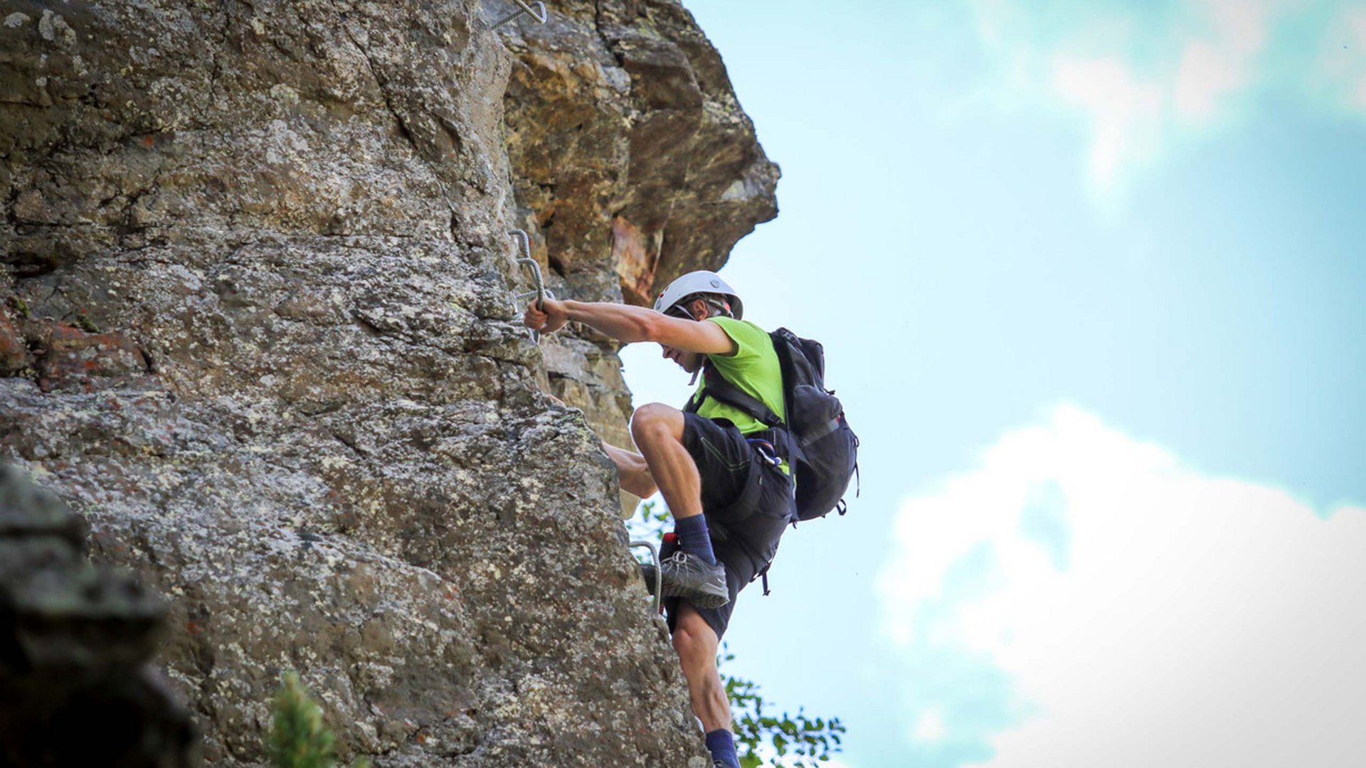Ihr Urlaub im Sporthotel in Tirol Mann klettert mit Helm und Rucksack an Felswand im Freien