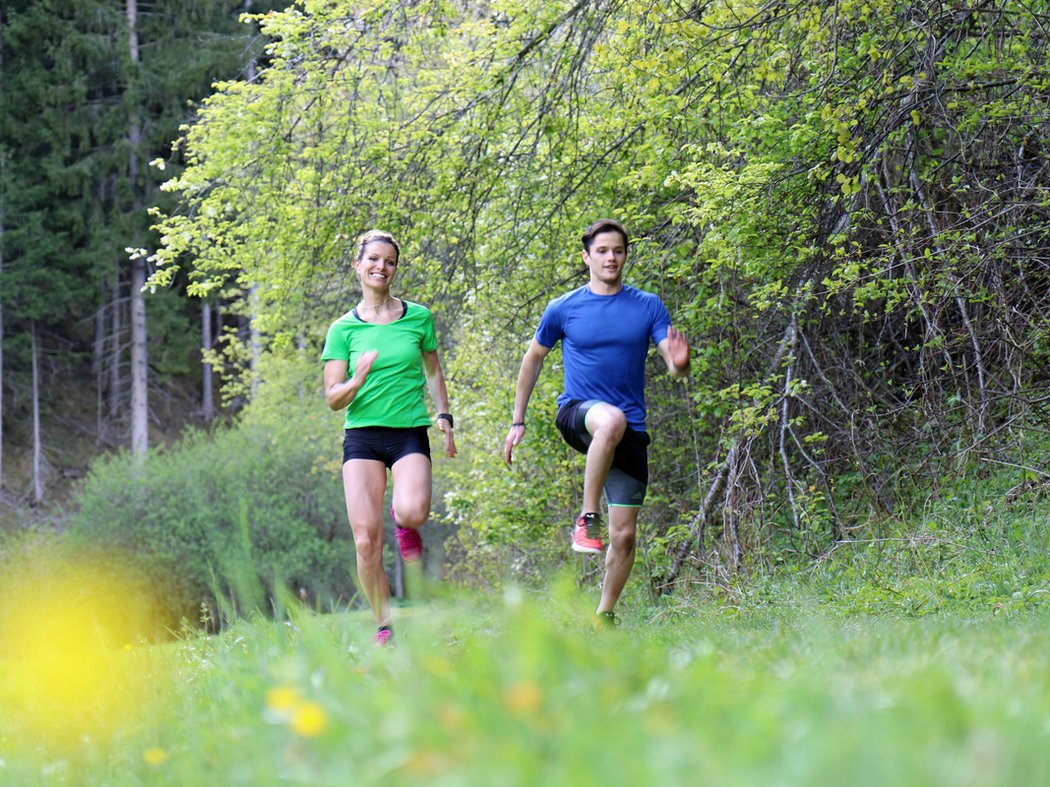 Between mountain peaks and river valleys Woman and man jogging in the forest on a sunny spring day