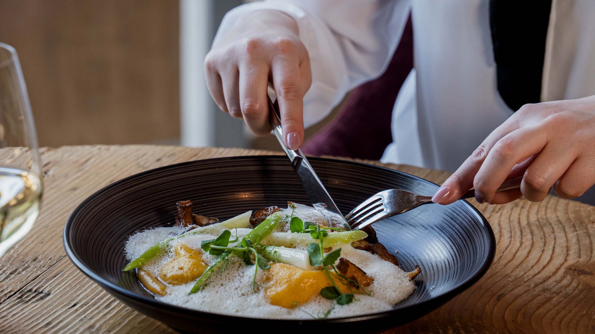 Looking for a hotel in Prutz? Person eating a dish with asparagus, mushrooms, and foam in a black bowl