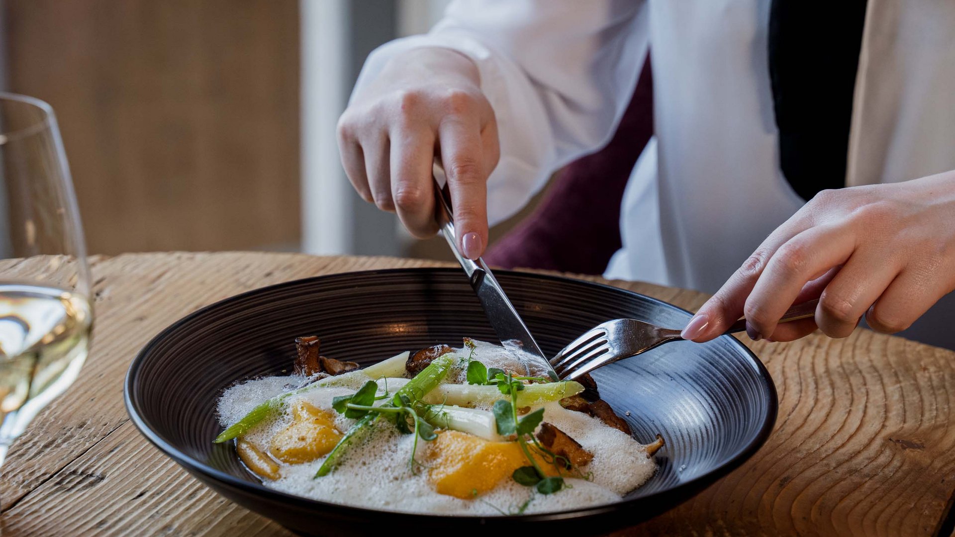 Ihr Wellnesshotel nahe der Schweizer Grenze Person isst ein Gericht mit Spargel, Pilzen und Schaum in einem schwarzen Teller