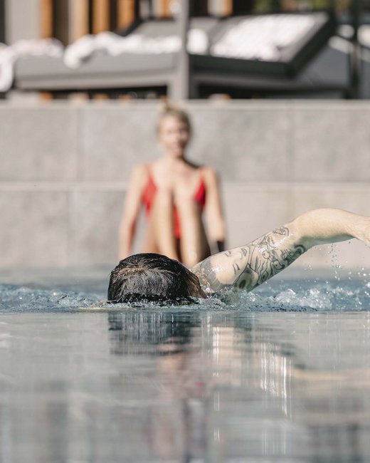 Feiern Sie Ihre Feste in Tirol Person mit Tattoo schwimmt im Pool, andere Person sitzt im Hintergrund