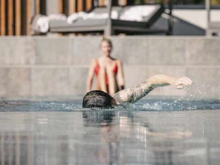 Looking for a hotel with spa in Tyrol? Tattooed person swimming in pool, another person sitting in background