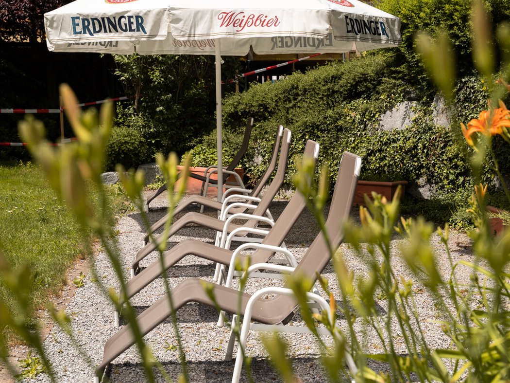 Der Sommer darf kommen! Leere Liegestühle unter einem Erdinger Weißbier-Sonnenschirm im Garten