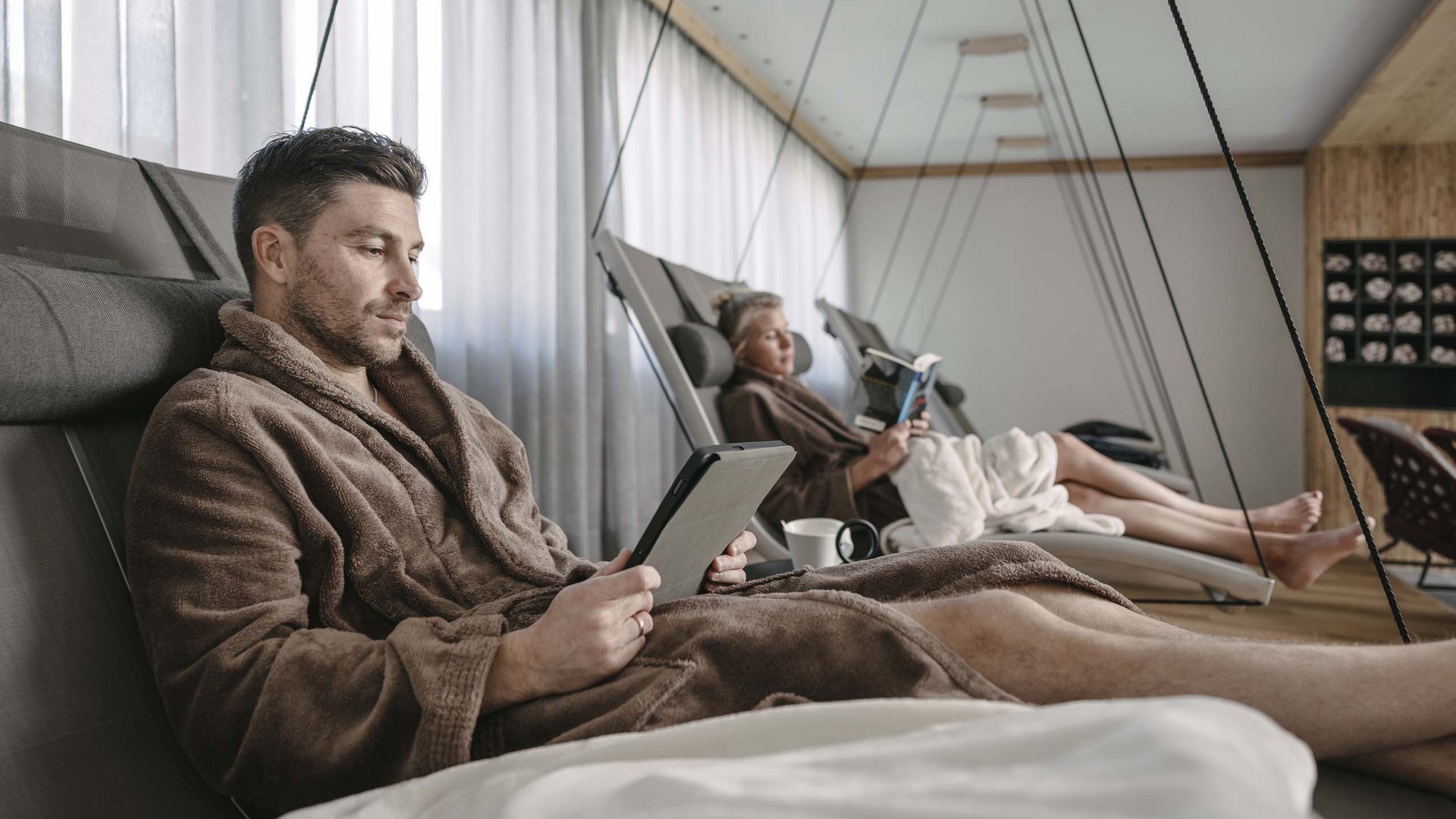 Looking for a hotel with spa in Tyrol? Two people relaxing in bathrobes on lounge chairs reading