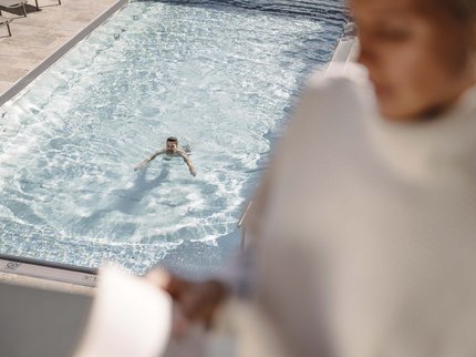 Looking for a hotel with spa in Tyrol? Person swimming in clear pool, another person blurred in foreground